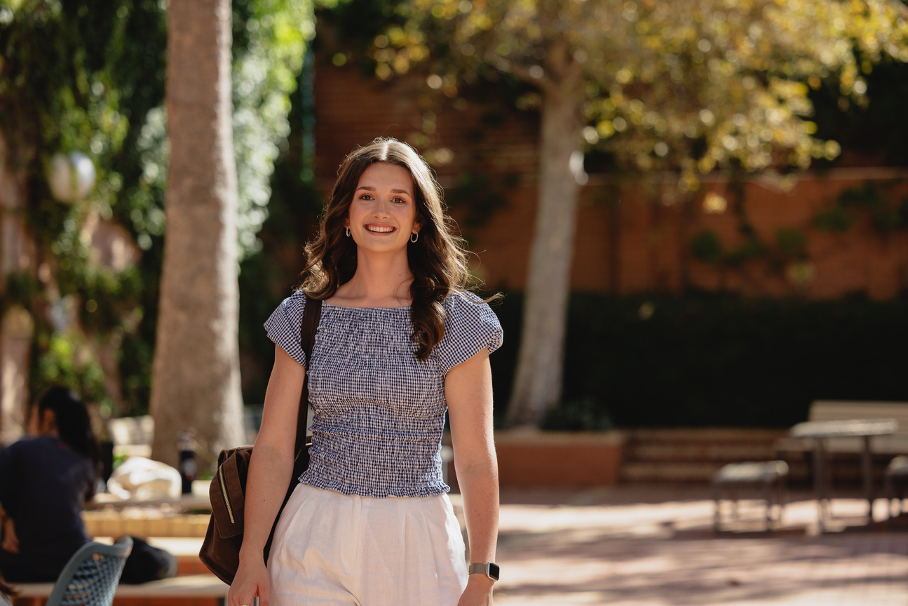 Notre Dame University student standing outside in a courtyard in the sun smiling at the camera. 