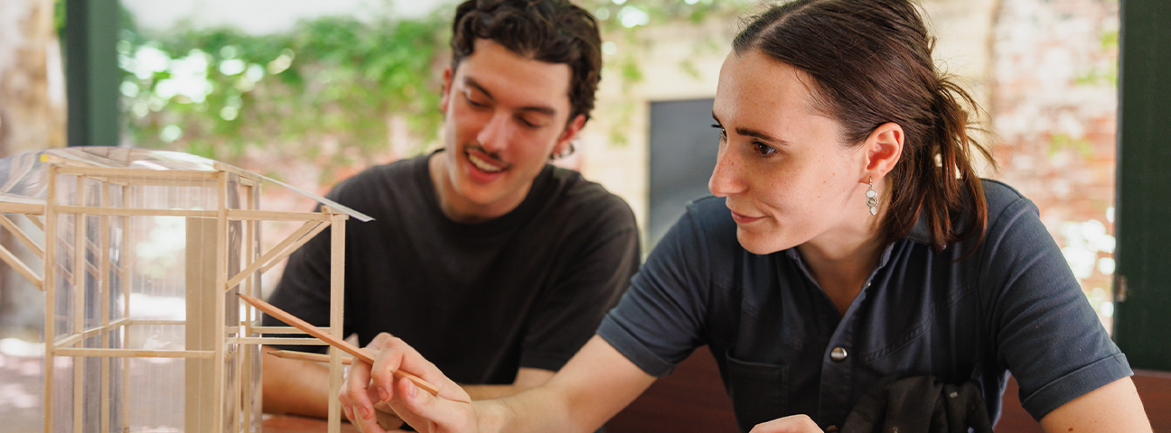 Two architecture students working on a project made of wooden sticks.  