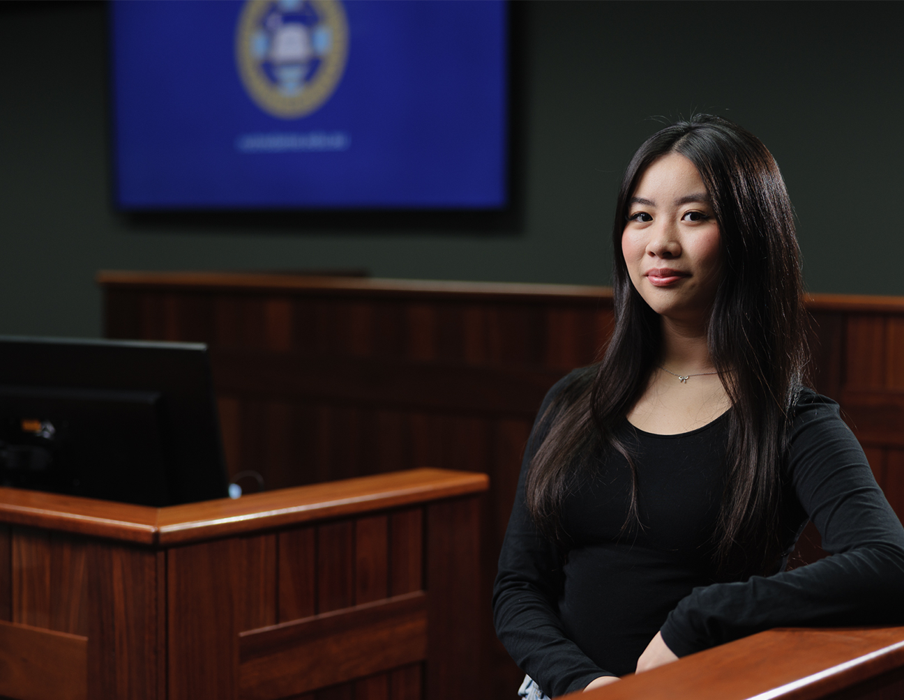 Female undergraduate law student leaning against a bench inside a lecture theatre. 