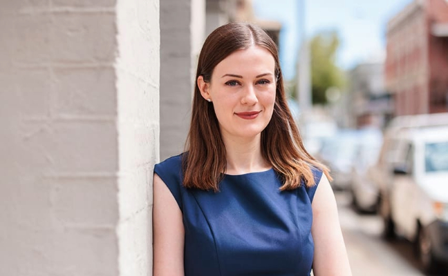 Notre Dame female medicine student wearing a dark blue dress leaning on a Fremantle campus building 