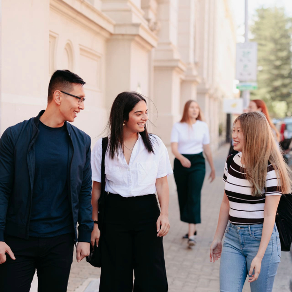 A group of three students walking down Fremantle campus chatting and smiling 