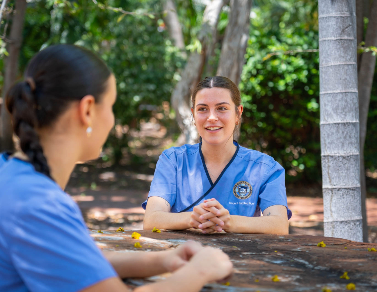 Female nursing student in a garden courtyard facing the camera and talking to another student