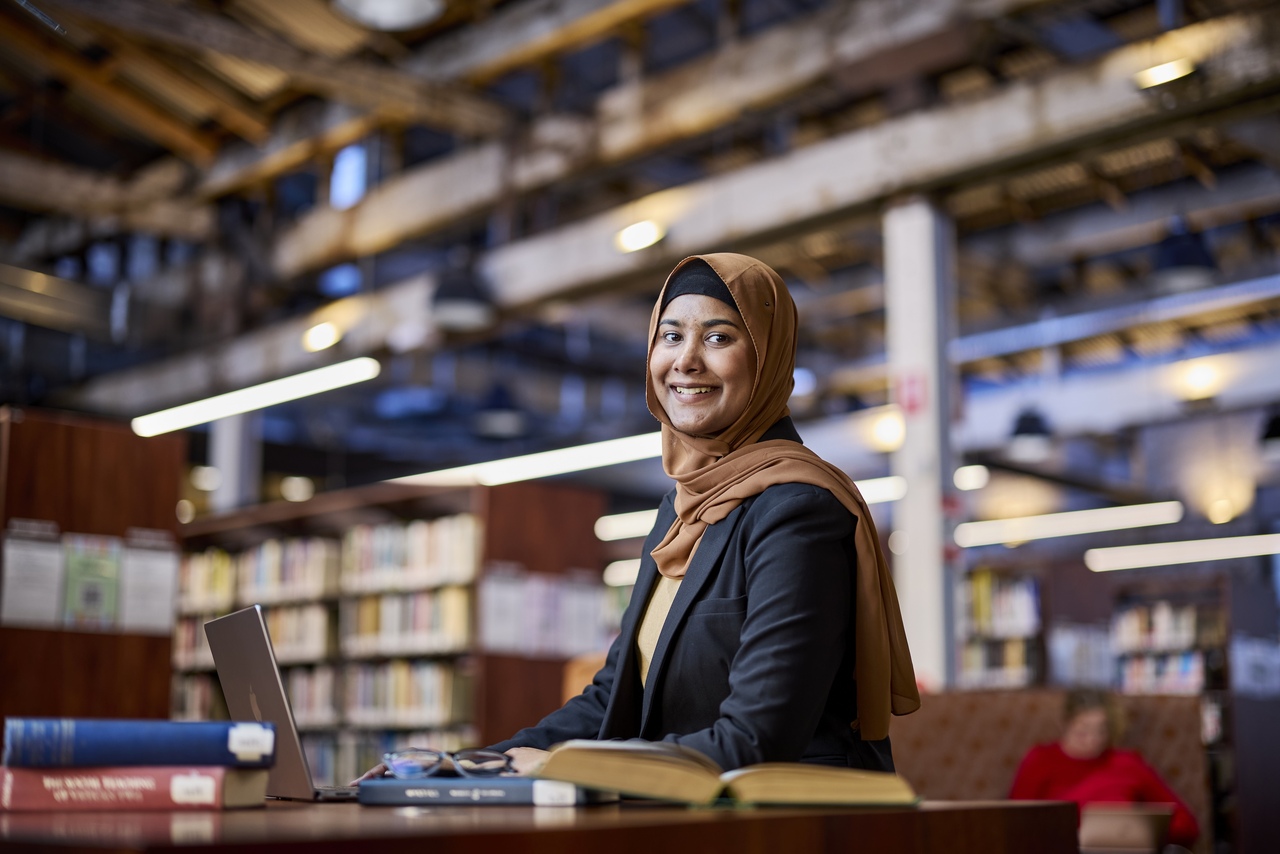 Notre Dame female undergraduate Nursing student sitting a library smiling at the camera.