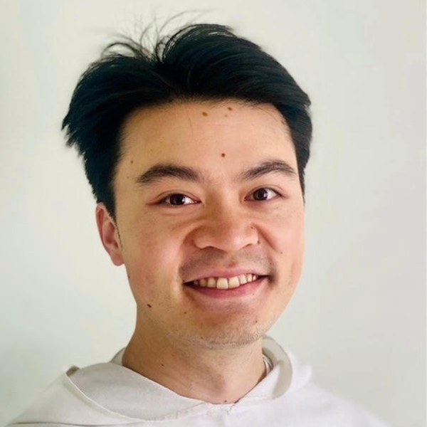 A man with short dark hair is smiling towards the camera in front of a cream coloured wall